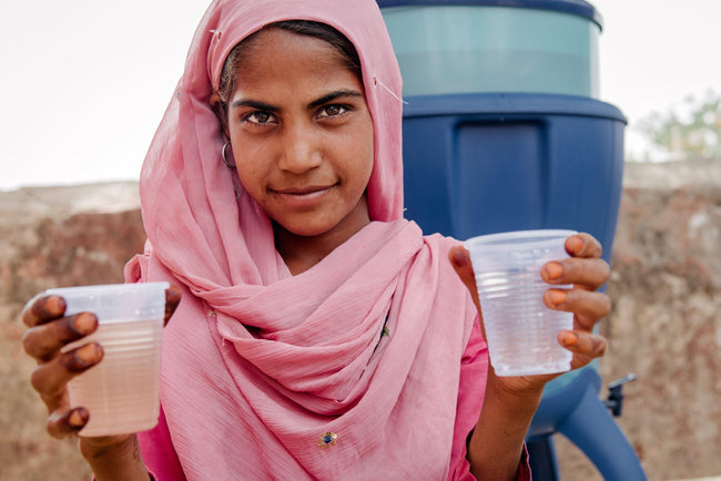 Girl holding two cups of safe water beside a LifeStraw Community purifier — Give safe water donations fund safe water